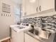 Modern laundry room with stainless steel sink, updated mosaic backsplash, and white cabinets at 8657 Aberdeen Cir, Highlands Ranch, CO 80130