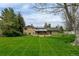 Expansive backyard view showcasing a brick home, large green lawn, mature trees, and outdoor patio space at 11310 W Center Ave, Lakewood, CO 80226