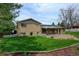 View of the home's rear exterior, featuring a brick facade, covered patio, and spacious green backyard, with mature trees at 11310 W Center Ave, Lakewood, CO 80226