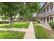 Well-maintained townhome with lush green lawn, mature trees, and a sidewalk leading to the entrance at 6495 E Happy Canyon Rd # 158, Denver, CO 80237