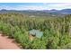 Aerial view of home with green roof surrounded by dense forest and mountains in the distance at 30122 Nancys Ln, Conifer, CO 80433