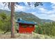 Hillside view of the red modern home, surrounded by lush greenery and trees at 5896 Peregrine Trl, Golden, CO 80403