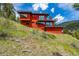 Hillside view of the modern red home, featuring large windows and sleek architectural design at 5896 Peregrine Trl, Golden, CO 80403