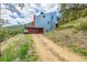 Modern home on a hillside with a metal facade and garage, accessible by a dirt driveway at 5896 Peregrine Trl, Golden, CO 80403