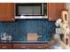 Close-up of kitchen with stainless steel microwave, wooden cabinets, and backsplash with decorative blue tiling at 8100 W 8Th Ave, Lakewood, CO 80214