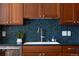 Kitchen features a stainless steel sink, wood cabinetry, stainless steel dishwasher, and backsplash with decorative blue tiling at 8100 W 8Th Ave, Lakewood, CO 80214