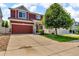 Two-story home featuring a red exterior, spacious driveway, two-car garage, and well-maintained lawn at 5558 Malta St, Denver, CO 80249