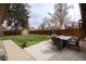 Manicured backyard featuring lush green grass, a stone patio, dining set and mature trees at 2250 N Monaco Pkwy, Denver, CO 80207