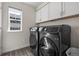 Modern laundry room featuring a black washer and dryer set, laminate flooring, and white storage cabinets at 7166 S Vandriver Way, Aurora, CO 80016