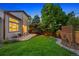Landscaped backyard with green grass, a stone patio, a wooden fence, and mature trees at twilight at 7114 S Acoma Way, Littleton, CO 80120
