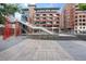 Exterior view of a modern brick apartment complex with pedestrian bridge access and landscaped plaza at 2100 16Th St # 600, Denver, CO 80202