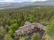 Expansive aerial view of a grand home with a paved driveway, surrounded by lush forest and distant mountain peaks at 12653 Rancho Ct, Conifer, CO 80433