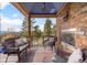 Covered outdoor deck featuring a stone fireplace, comfortable seating, and picturesque views of the surrounding landscape at 12653 Rancho Ct, Conifer, CO 80433