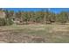 Wide shot of the home surrounded by lush landscaping, mature trees, and an open field at 1559 Apex Rd, Franktown, CO 80116
