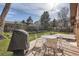 Outdoor dining set with grill on a concrete patio in a beautiful backyard with lush lawn and mature trees at 8122 W Woodard Dr, Lakewood, CO 80227