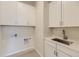 Bright laundry room features white cabinetry, stainless steel sink, and wood-look tile flooring at 11454 Stonewash St, Littleton, CO 80125