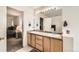 A well-lit bathroom featuring double sinks, wood cabinets, and a view into the bedroom at 20000 Mitchell Pl # 51, Denver, CO 80249