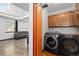 Laundry room with modern washer and dryer units, wood cabinets, and access to living room at 3907 E 133Rd Ct, Thornton, CO 80241