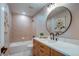 Elegant bathroom featuring a round mirror, vanity with light wood cabinets, and a tub with a tiled wall surround at 5597 S Buchanan St, Aurora, CO 80016