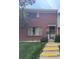 A classic brick townhome featuring a well-manicured lawn, contrasted by yellow-striped steps that lead to the front door at 8779 Santa Fe Dr, Thornton, CO 80260