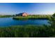 Picturesque red barn-style building overlooking a serene lake with lush green surroundings under a clear blue sky at 16602 E 109Th Ave, Commerce City, CO 80022