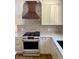 Updated kitchen featuring white cabinets, wood accent vent hood, and gas range at 9810 Venneford Ranch Rd, Highlands Ranch, CO 80126