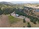 Expansive aerial view of a property with a large blue barn, vineyard, sheds, and surrounding wooded hills at 1044 S Grapevine Rd, Golden, CO 80401