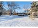 This snowy backyard has mature trees and a single-story house with a sunroom at 8530 W Jefferson Ave, Denver, CO 80235