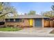 Single-story brick home with a well-kept lawn, a driveway, and a pop of color from the yellow front door at 6742 Marshall St, Arvada, CO 80003