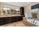 Elegant bathroom featuring dark wood cabinets, a large mirror, and a luxurious soaking tub near a window at 14582 Homestead Pl, Broomfield, CO 80023