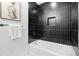 Modern bathroom featuring a white bathtub, sleek black tile surround, and a convenient recessed shelf at 3519 S Holly St, Denver, CO 80237