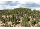 The aerial view captures the house amidst a forest, highlighting its idyllic and private setting at 7290 Timber Trail Rd, Evergreen, CO 80439