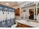 Well-lit bathroom featuring a blue patterned shower curtain, wooden cabinet, and white countertop at 1805 Parkdale N Cir, Erie, CO 80516