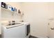 Bright laundry room featuring a modern white washer and dryer, complemented by a shelf for storage at 18242 E Bethany Pl, Aurora, CO 80013