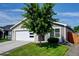 Charming home featuring a modern garage door, gray siding, green lawn, and a large tree in the front yard at 719 S Hoover Ave, Fort Lupton, CO 80621