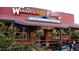 Exterior view of Woody's Wood Fired Pizza with outdoor seating and vibrant hanging plants at 19067 W 57Th Dr, Golden, CO 80403