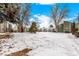 View of townhomes surrounded by mature trees and a large, snow-covered front yard at 4950 Homestead Pl # 23, Thornton, CO 80229