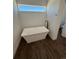 Modern bathroom with standalone soaking tub under a window and dark wood-look flooring at 59440 E 56Th Ave, Strasburg, CO 80136