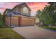Inviting two-story home featuring a three-car garage, brick accents, and well-maintained landscaping under a beautiful sunset sky at 10089 Wynwood Way, Highlands Ranch, CO 80126