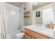 Well-lit bathroom with a shower-tub combo, white tile, and a vanity with wooden cabinets at 12705 Ulster St, Thornton, CO 80602