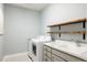 Well-equipped laundry room with modern appliances, gray cabinets, floating wood shelves, and a sink with faucet at 27653 E Euclid Dr, Aurora, CO 80016