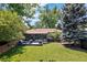 A large backyard featuring a deck, lush lawn, mature trees, and a wooden fence at 5525 E Bails Dr, Denver, CO 80222