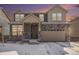 Two-story home with stone accents, an attached two-car garage, and snow-covered front yard at dusk at 16278 E 111Th Pl, Commerce City, CO 80022