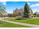 A bright and sunny home featuring a lush lawn, stone accents, and a mature evergreen tree at 27290 E Nova Cir, Aurora, CO 80016