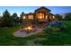 Beautiful backyard at dusk featuring a fire pit, patio, lush lawn, mature trees, and uplighting at 4651 Sonado Pl, Parker, CO 80134