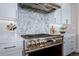 Gas range with decorative backsplash and modern hood, complemented by white cabinets and dark hardware at 2144 Bellcove Dr, Castle Pines, CO 80108