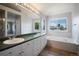 Bathroom featuring double sinks, a large mirror, and a soaking tub beneath a bright window at 17235 Opal Hill Dr, Parker, CO 80134