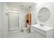 Bright bathroom with white wainscoting, shower, vanity, round mirror, and cabinet storage at 7527 E Severn Pl, Denver, CO 80230