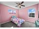 Cute pink bedroom with a ceiling fan, two windows with a backyard view, and playful decor at 9501 Richfield St, Commerce City, CO 80022