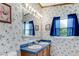 Bathroom with wallpaper, mirror, wood cabinet with blue tile, white sinks, and a bright window with blue curtains at 6310 W County Road 4, Berthoud, CO 80513